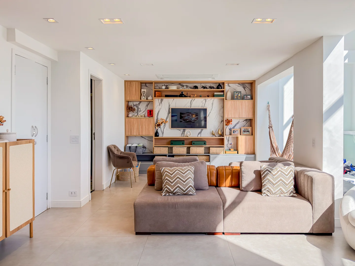 Sala integrada com sofá claro, painel de madeira e decoração em tons naturais