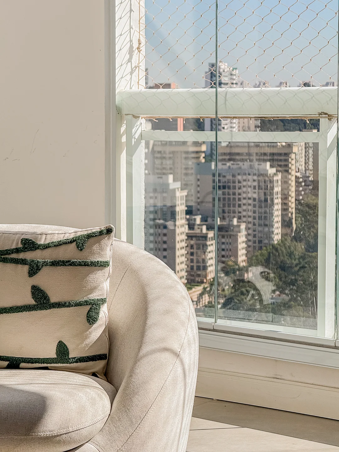Detalhe de sofá e almofadas junto à janela com vista da cidade